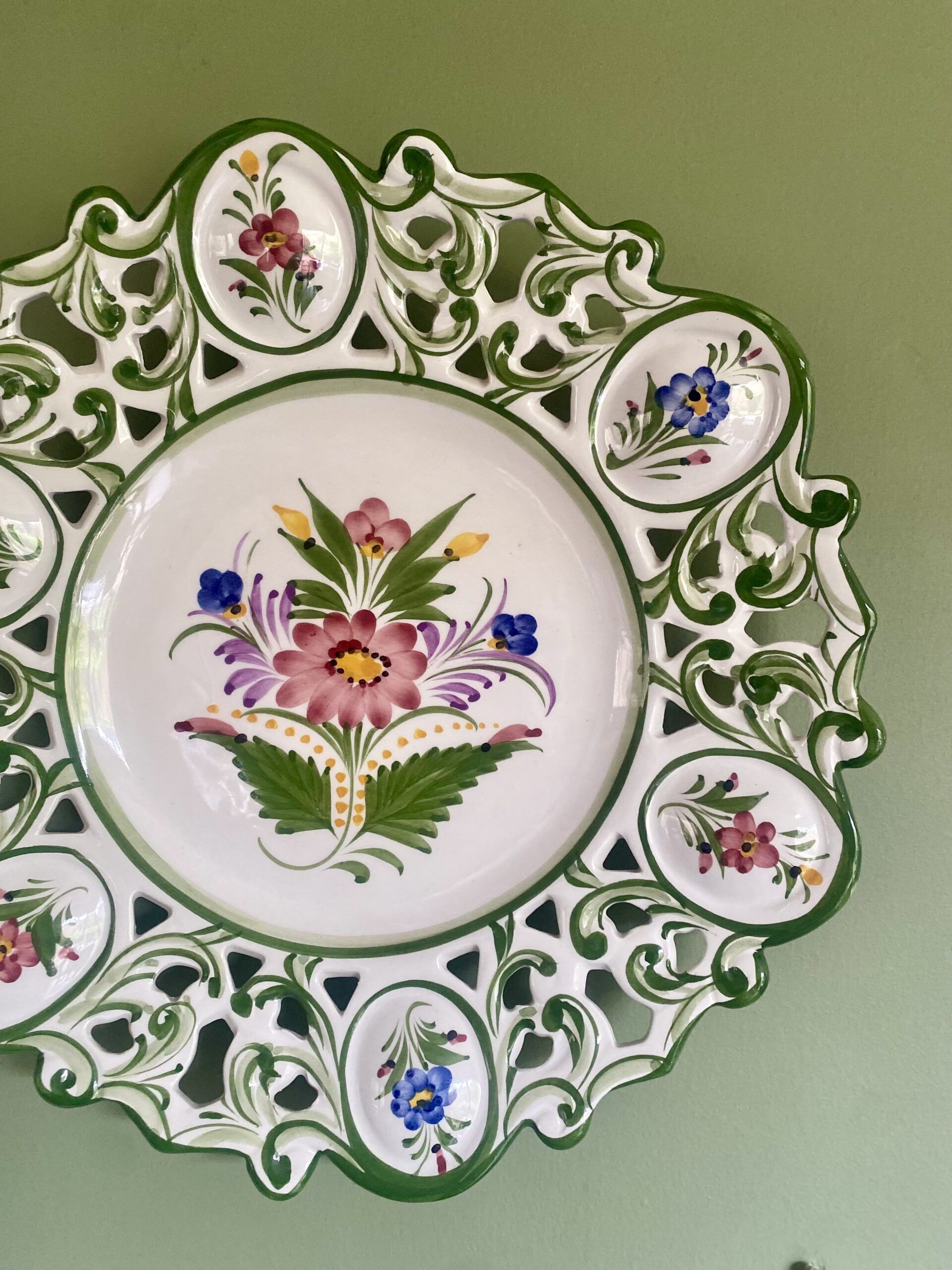 A hand-painted Portuguese wall plate with floral decoration hung against a green wall.
